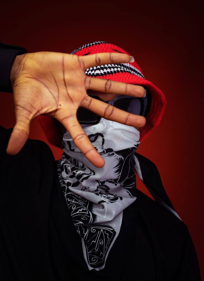 Stylish portrait of a man in a red hat, bandana, and sunglasses posing dramatically indoors.